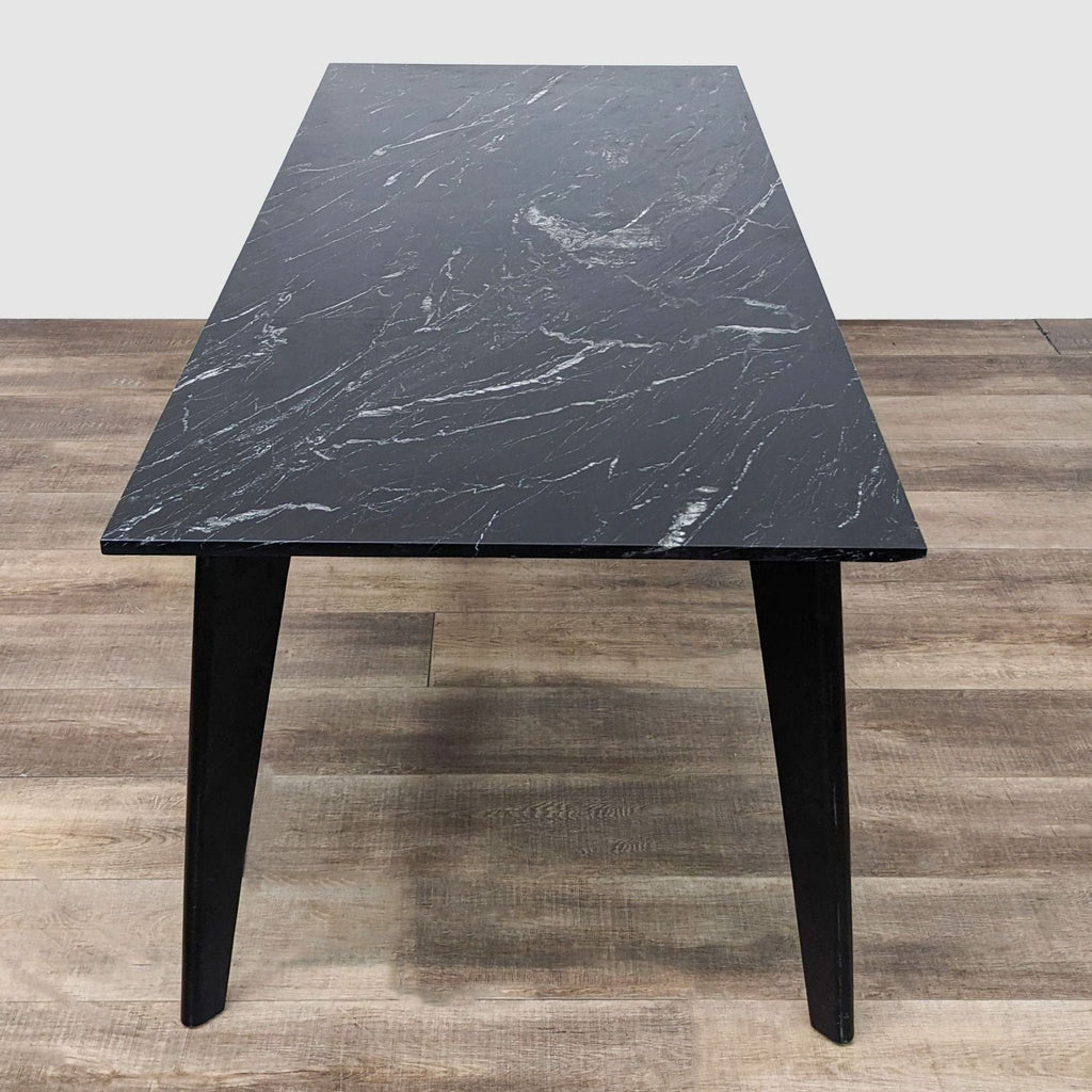 Angled view of CB2 Harper Dining Table showcasing the tapering steel legs and marble surface with distinctive grey and white patterns.