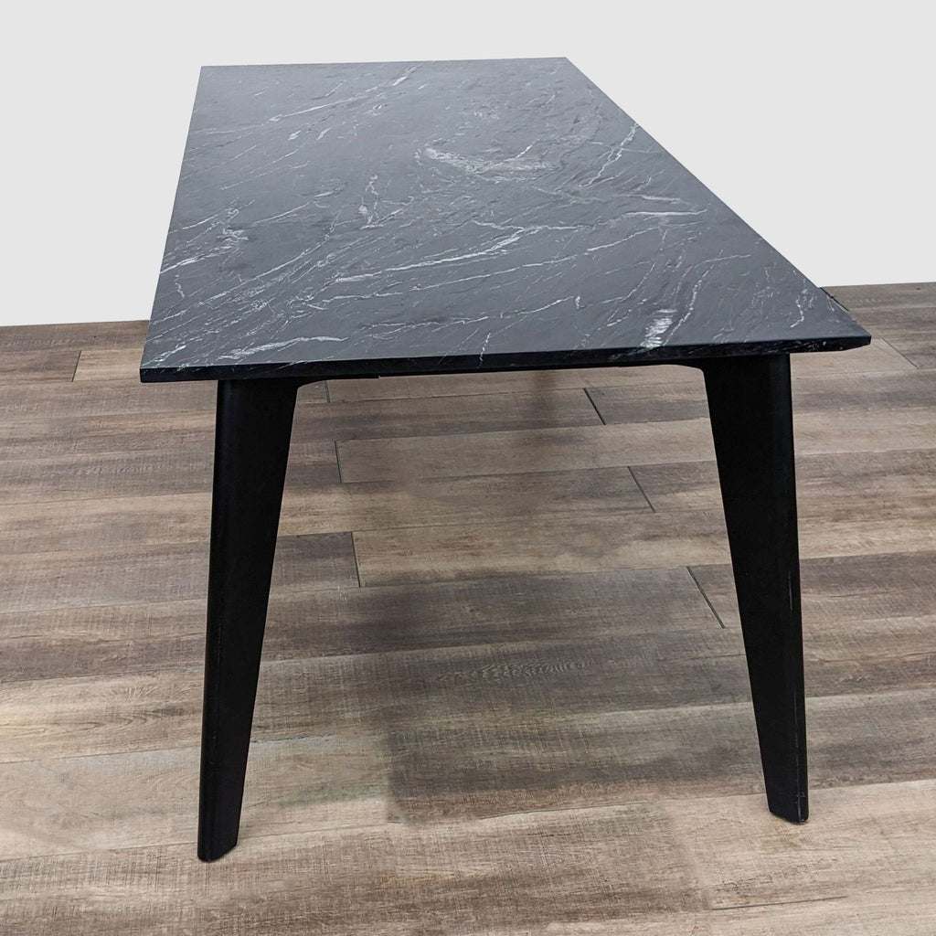 Close-up angled perspective on the Harper Dining Table by CB2 highlighting the marble top veining and sleek black steel legs.