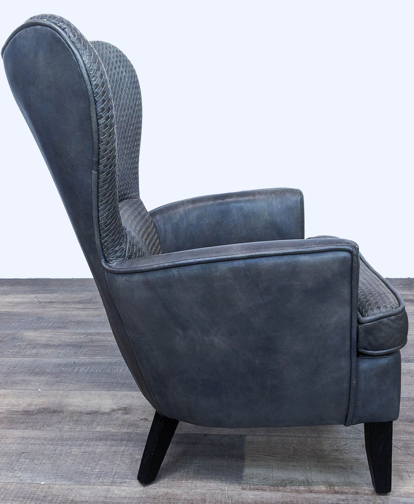 Side angle of a dark leather wingback Mentor chair by Timothy Oulton, showcasing the contrast of woven and smooth leather.