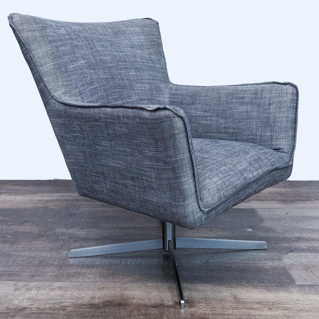3. The back angle of the Four Hands Jacob Chair with a curved design in gray fabric on a modern silver swivel base against wood flooring.