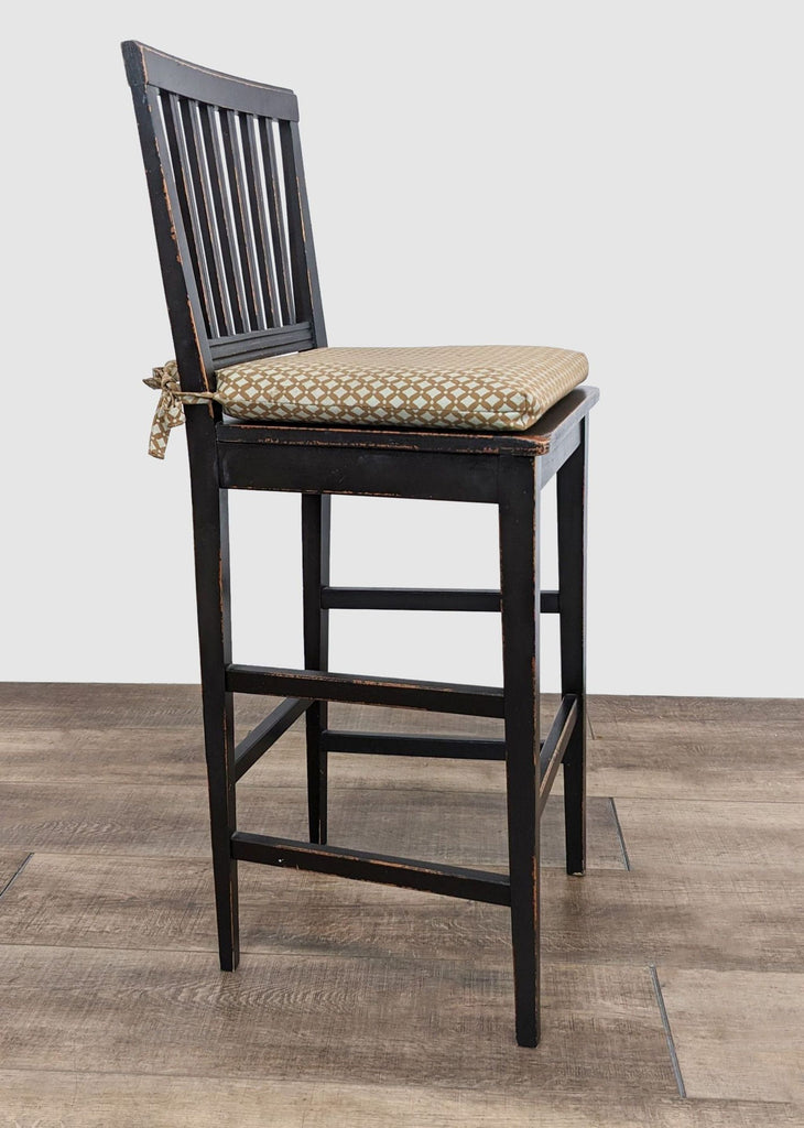 A single rail back barstool featuring chipped black paint, solid build, and a tied cushion by Crate and Barrel.