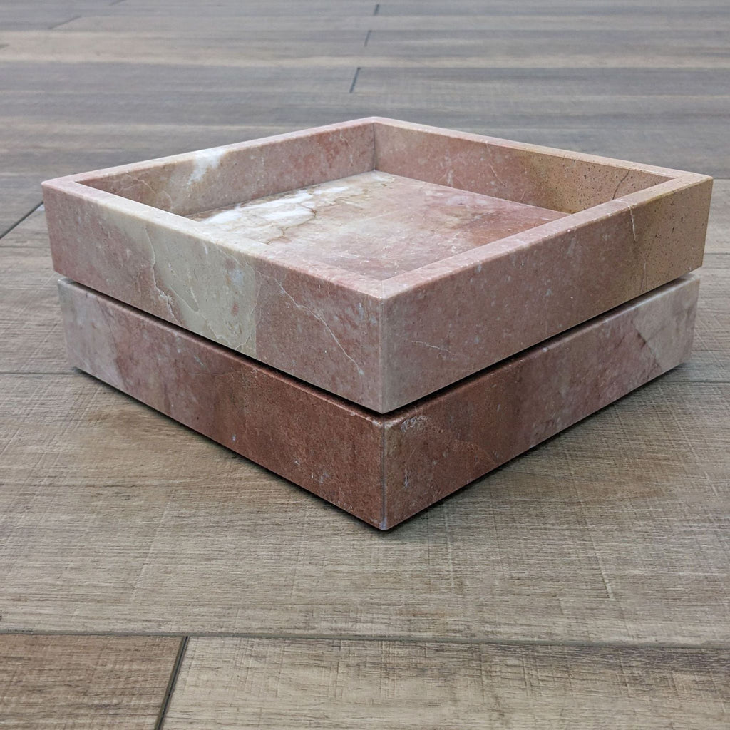 Two pink marble display trays by CB2 stacked on top of each other, placed on a wooden surface.  