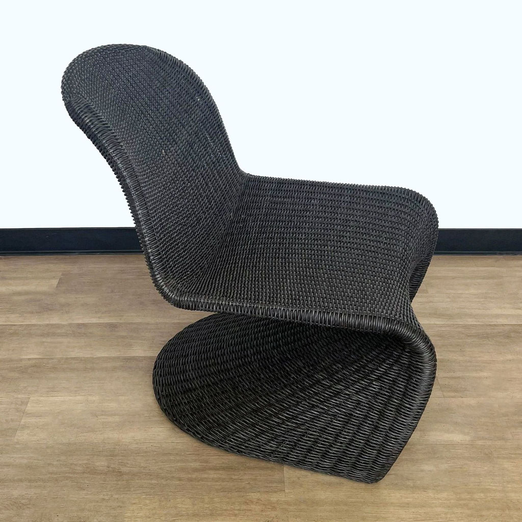 Stylish curved wicker lounge chair by Reperch, shown in side view on wooden floor.