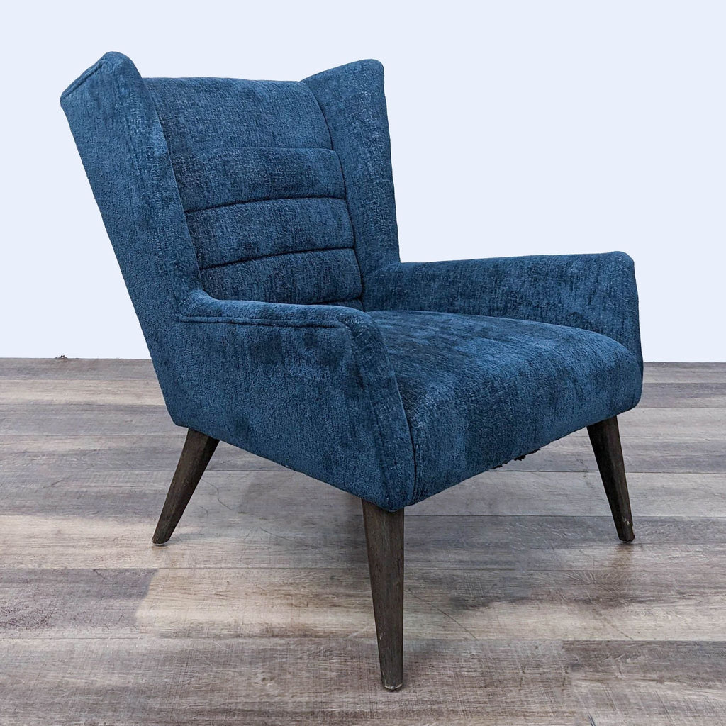 Side perspective of a retro-inspired blue wing chair by Four Hands with tufted channels and angled wooden legs.