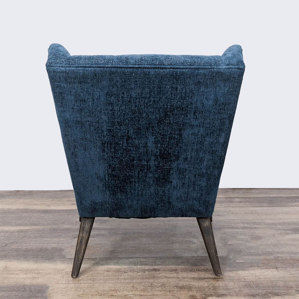 Rear angle showing the back of a textured blue Hollis Chair by Four Hands with a tufted upholstery and wooden leg silhouette.