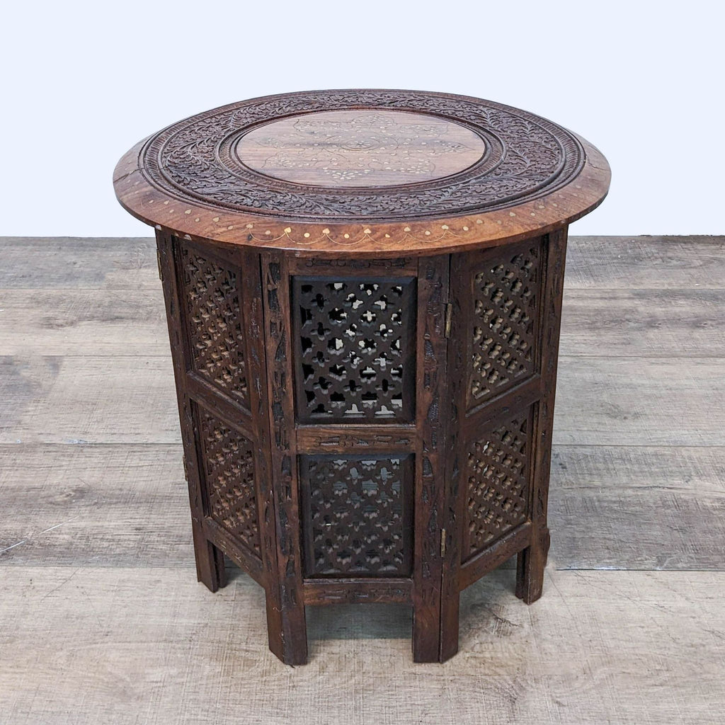 1. World Market side table with intricately carved body and brass inlay on top, displayed on a wooden floor.
