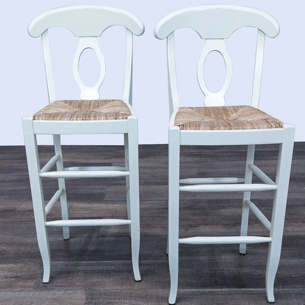 1. Two ivory-painted wooden barstools with curved backs and rush seats against a wood floor backdrop.