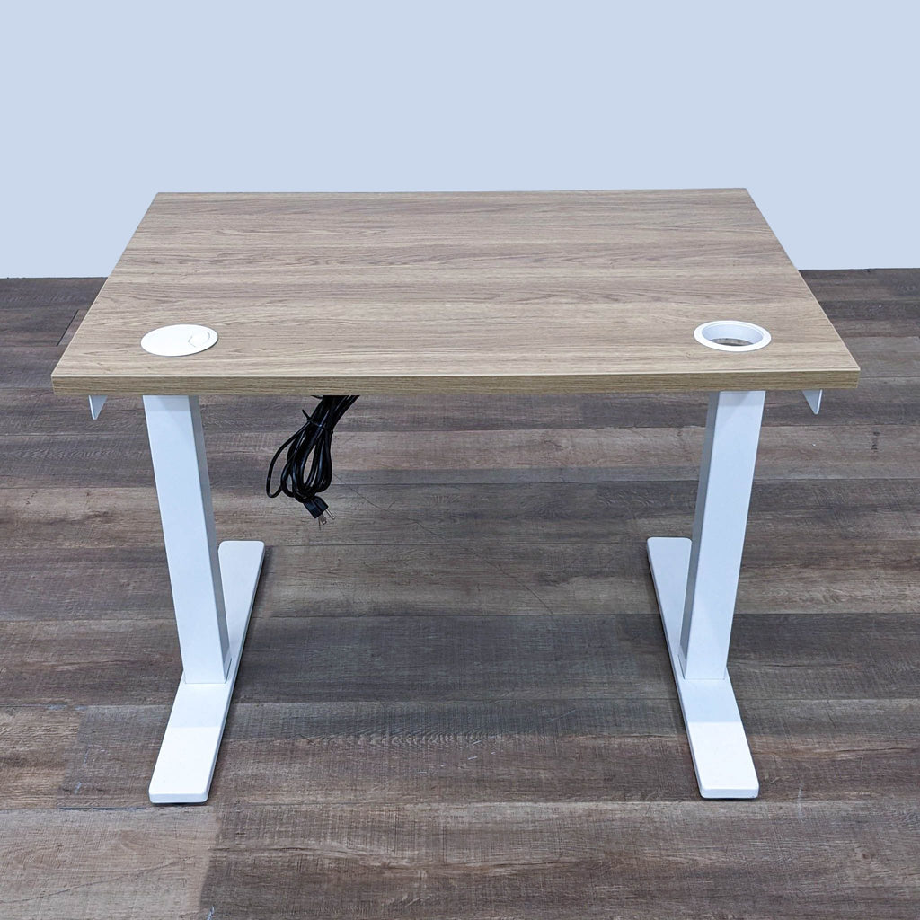 Fully's adjustable desk set at a medium height, wooden top with cable management holes, on wood floor.