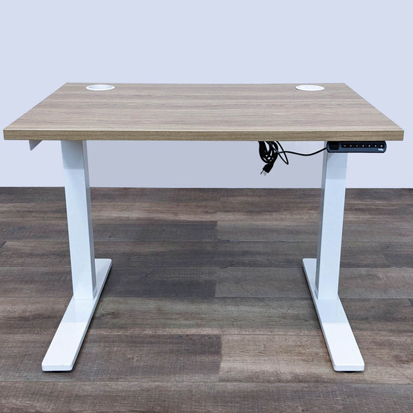 Fully brand adjustable desk at its lowest height, with wooden top and white legs on a wooden floor.
