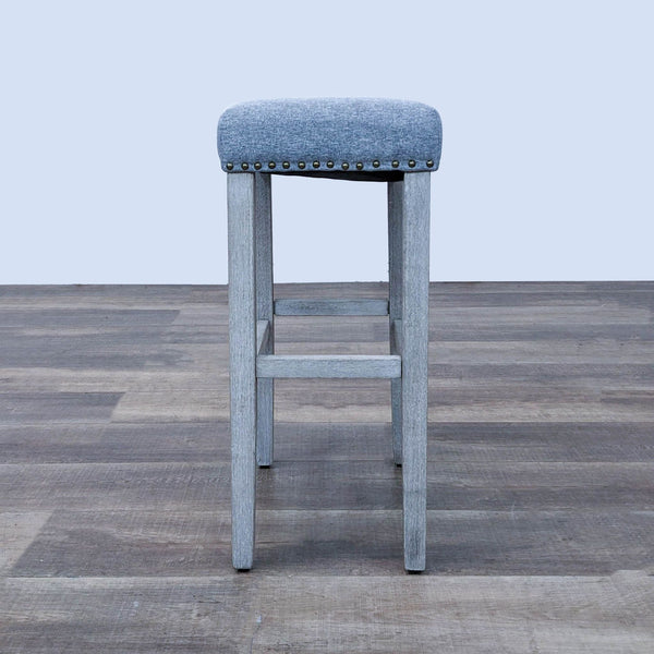 Gray padded barstool by Reperch with nailhead detail on a wood frame.