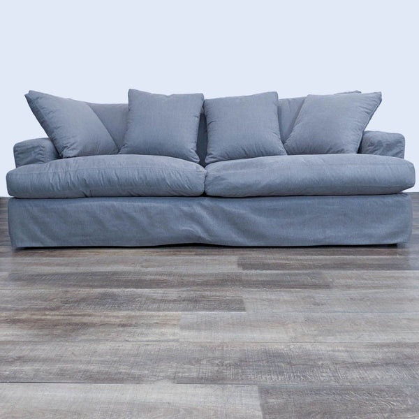 a grey sofa with a large cushion on a wooden floor.