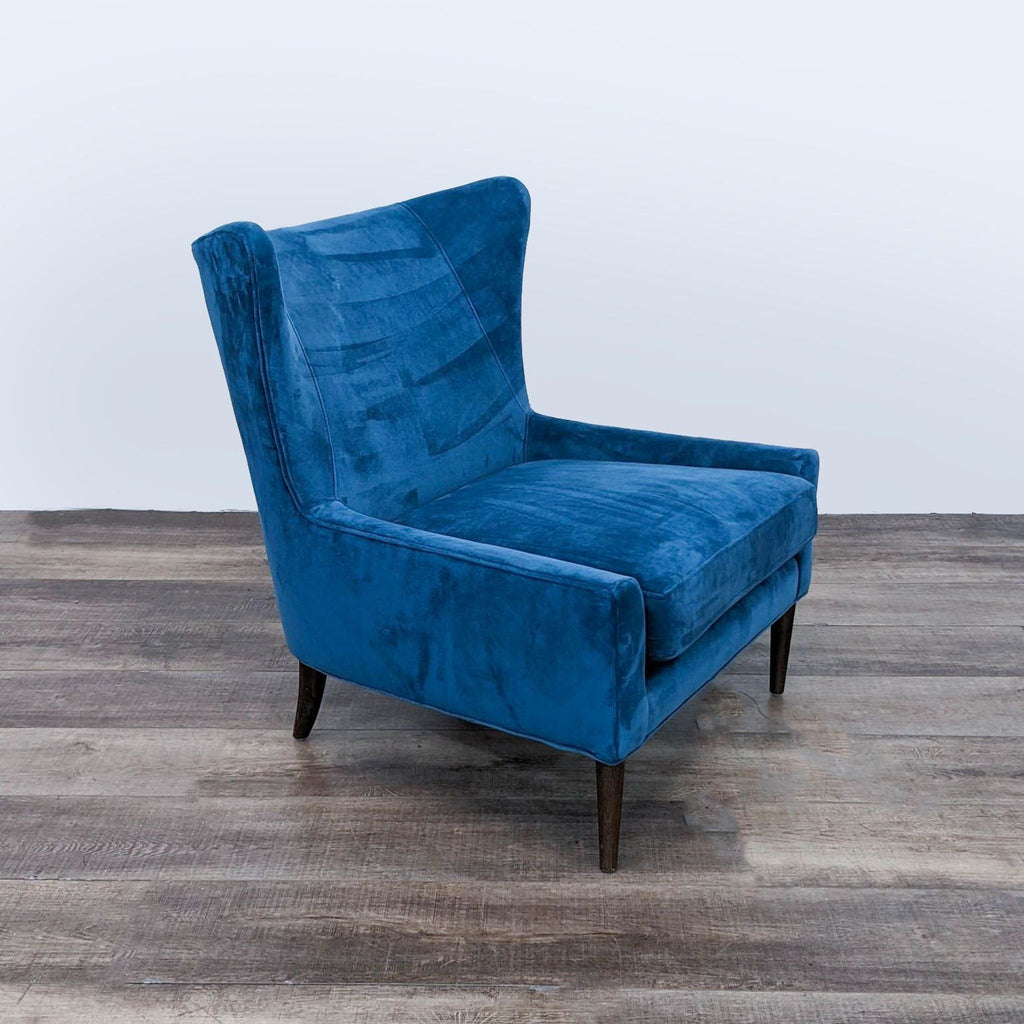 Angled view of Four Hands Marlow blue velvet wingback chair, with cushioned seat and dark wood tapered legs.