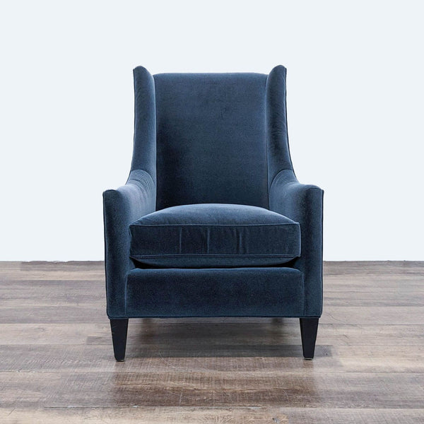 a blue velvet wingback chair with a black base and a white background.