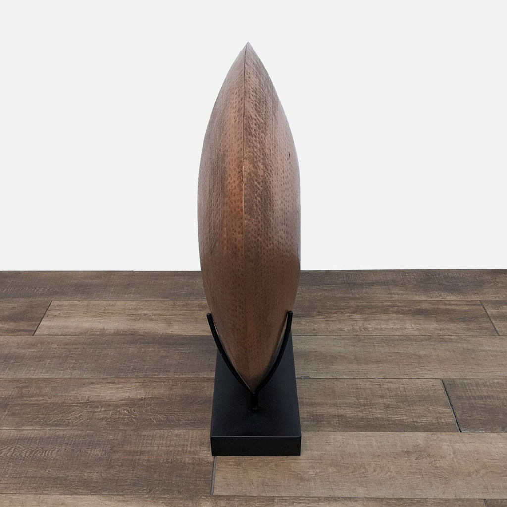 Side view of copper-plated disc vase on black stand, showcasing its sleek profile.