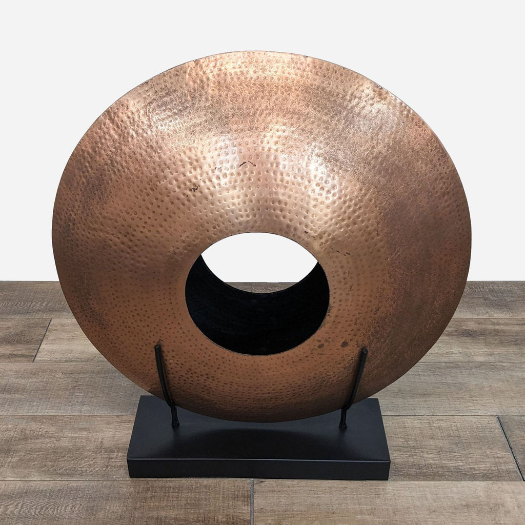 Close-up of circular copper vase with hammered texture, mounted on a stand.