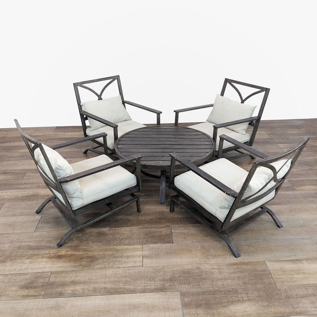Four metal armchairs with cushions and a round table form an outdoor set by Orchard.
