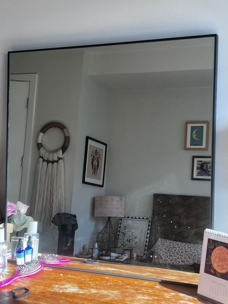 1. Pottery Barn square mirror with thin black frame, shown on a wooden vanity reflecting a cozy bedroom scene.