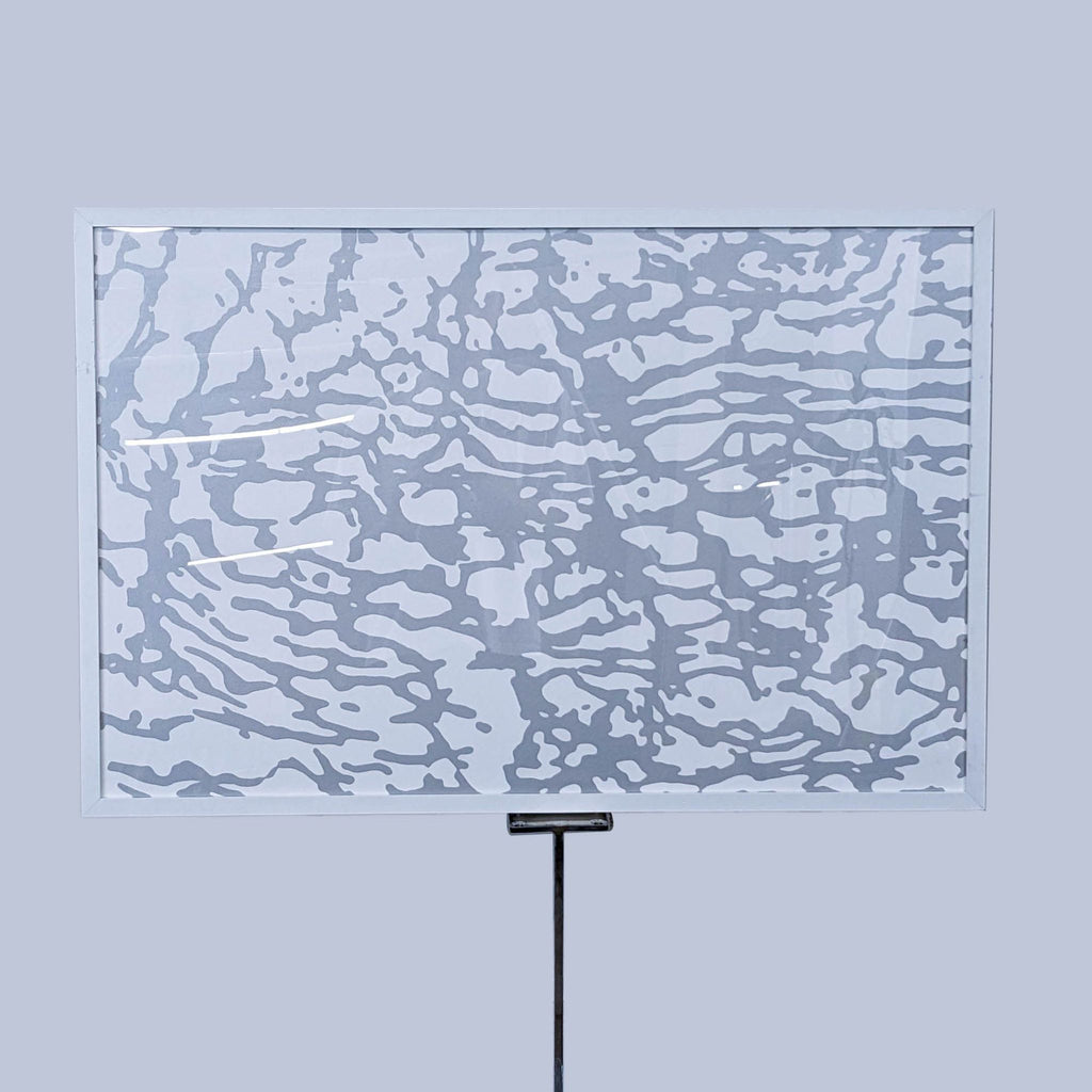 Abstract gray and white art in frame on stand.