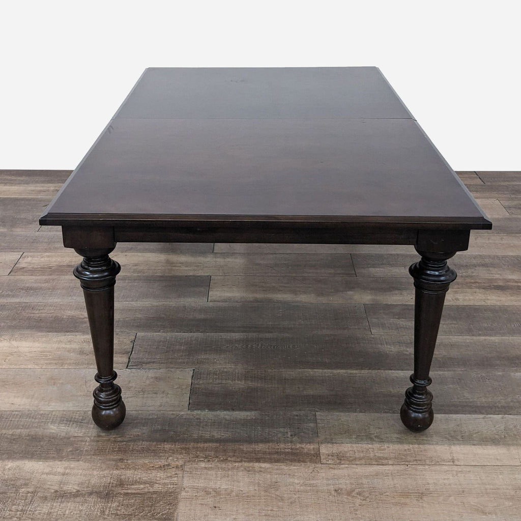 a dark brown wood dining table with a single leg.