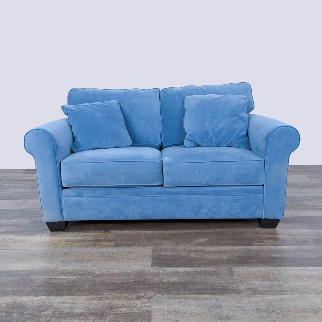 a blue sofa with two pillows on a wooden floor.