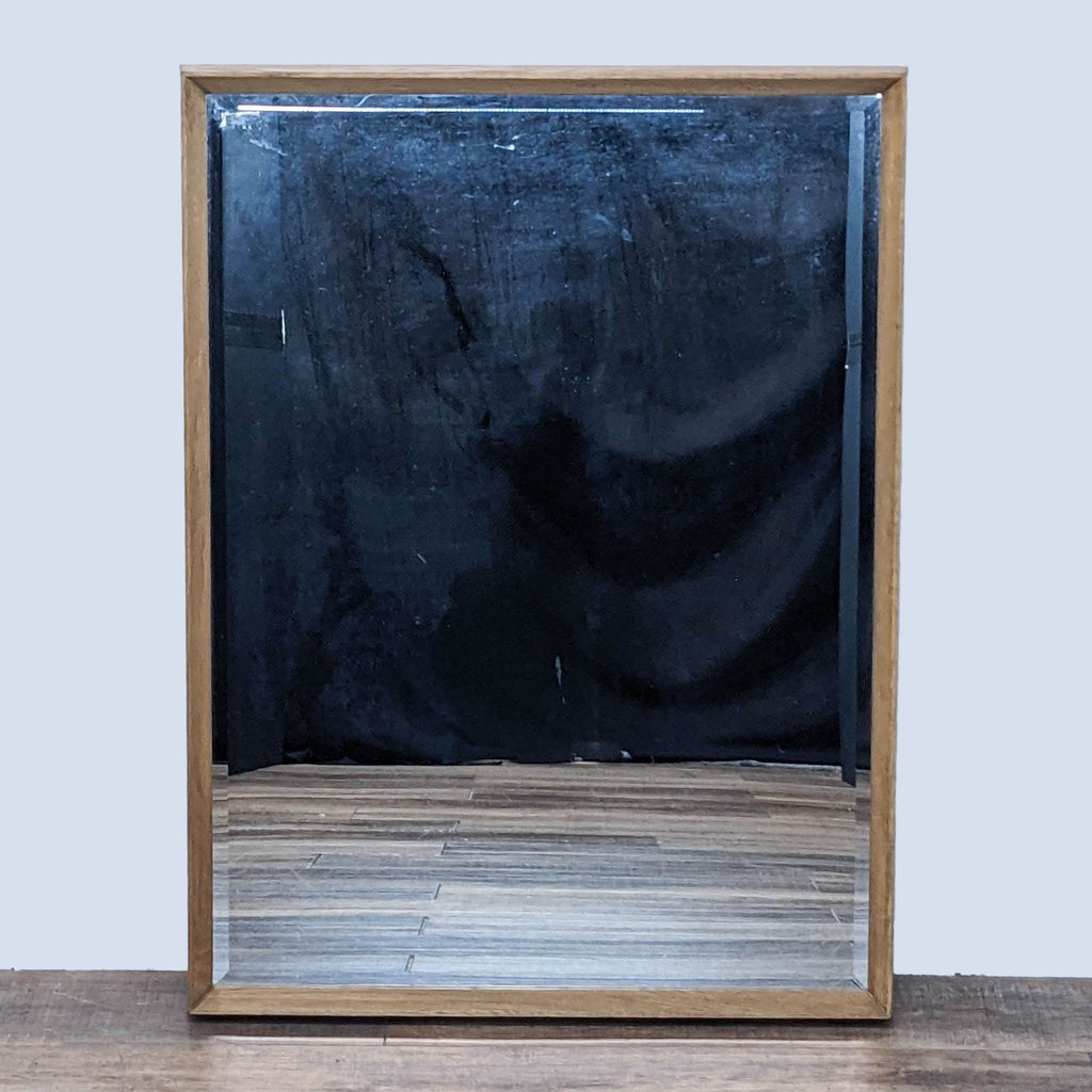 Beveled mirror with oak wood frame on a wooden floor background.