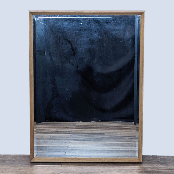 Beveled mirror with oak wood frame on a wooden floor background.