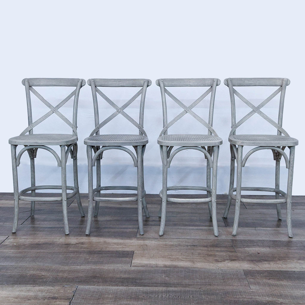 Four grey barstools with cane seats and cross-back detailing against a neutral background.