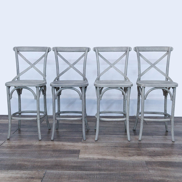 Four grey barstools with cane seats and cross-back detailing against a neutral background.