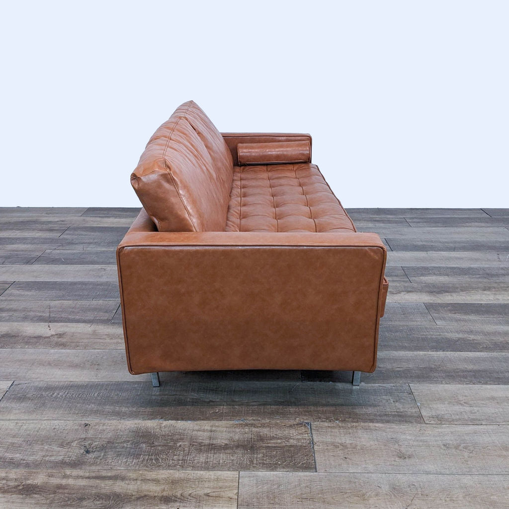 Side view of tufted leather sofa with bolster pillows and metal legs.  