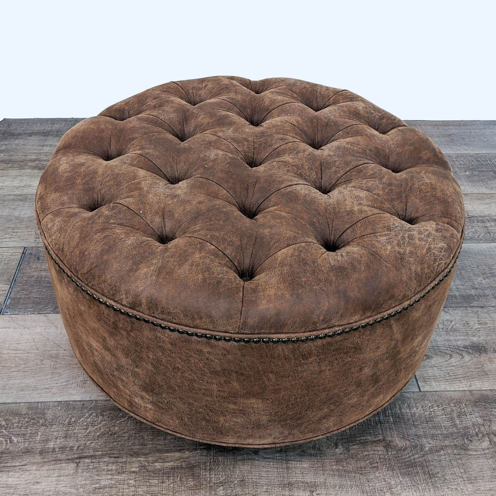 Brown leather tufted round ottoman with nailhead trim and dark wood feet.