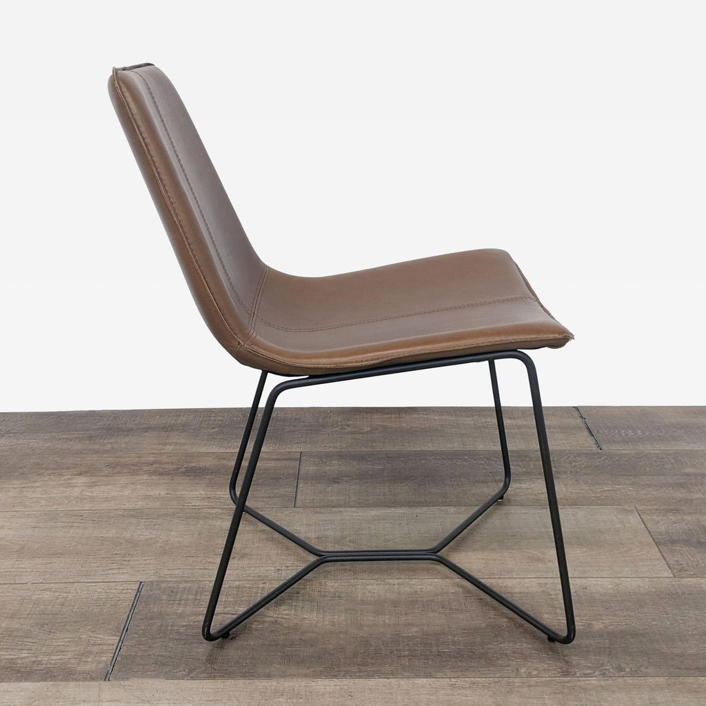 Side view of a brown leather dining chair with slim black metal legs on a wood floor.