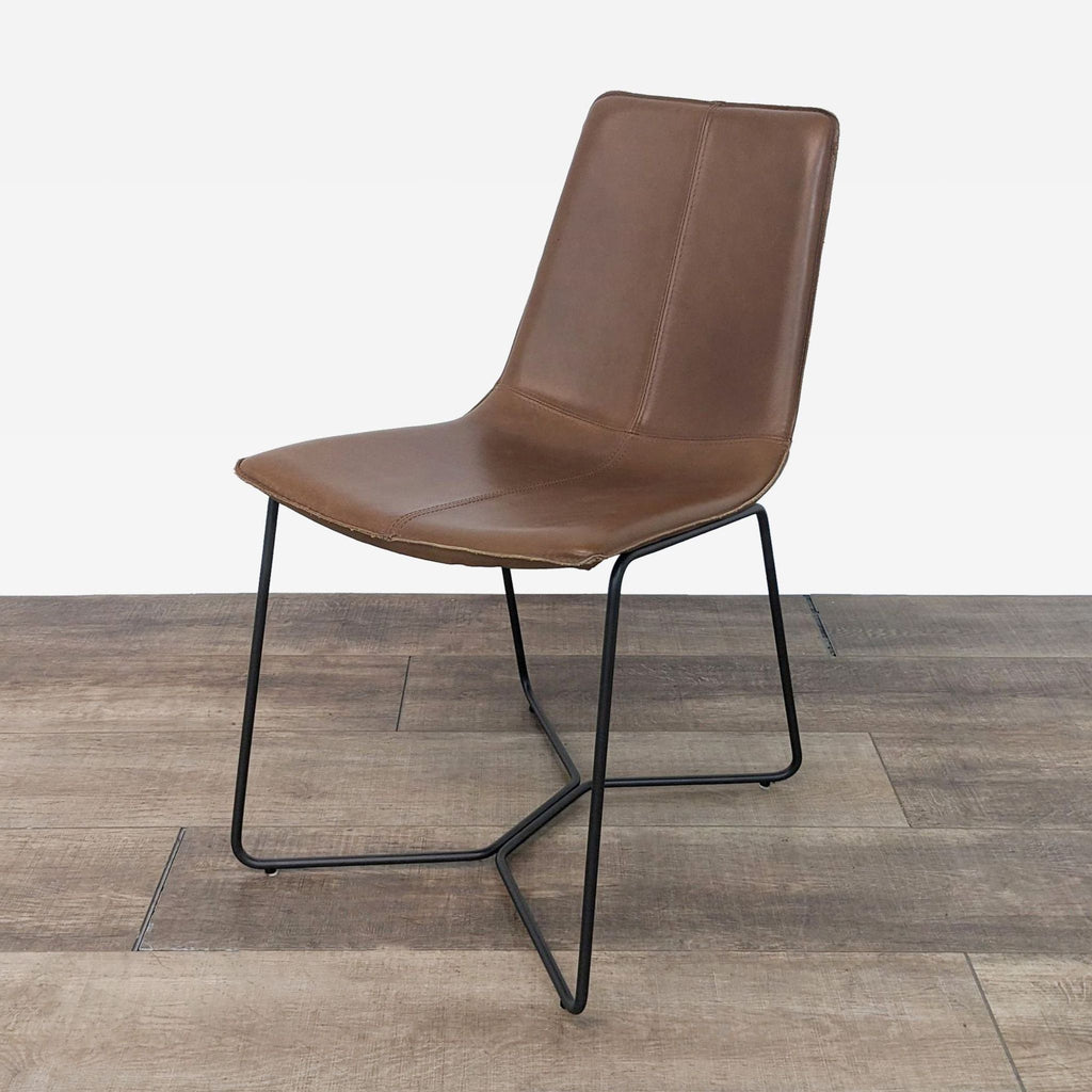 Angled view of a brown leather dining chair with a sleek design and black metal legs on a wooden surface.
