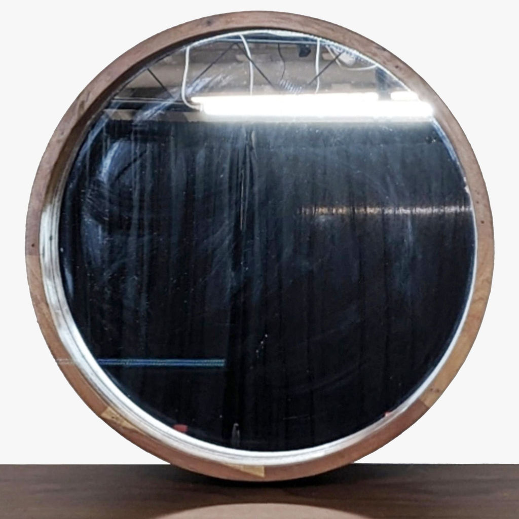 Round mirror from CB2 with an acacia wood frame, shown from the front, reflecting a dark background.