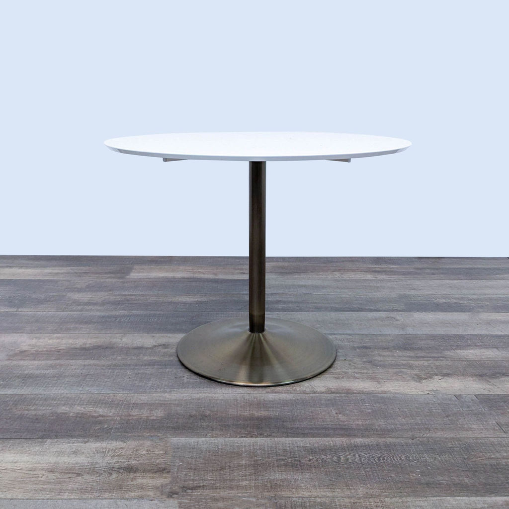 CB2 Odyssey Dining Table with white top and brass pedestal on wood floor.  