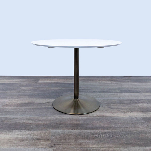 CB2 Odyssey Dining Table with white top and brass pedestal on wood floor.  