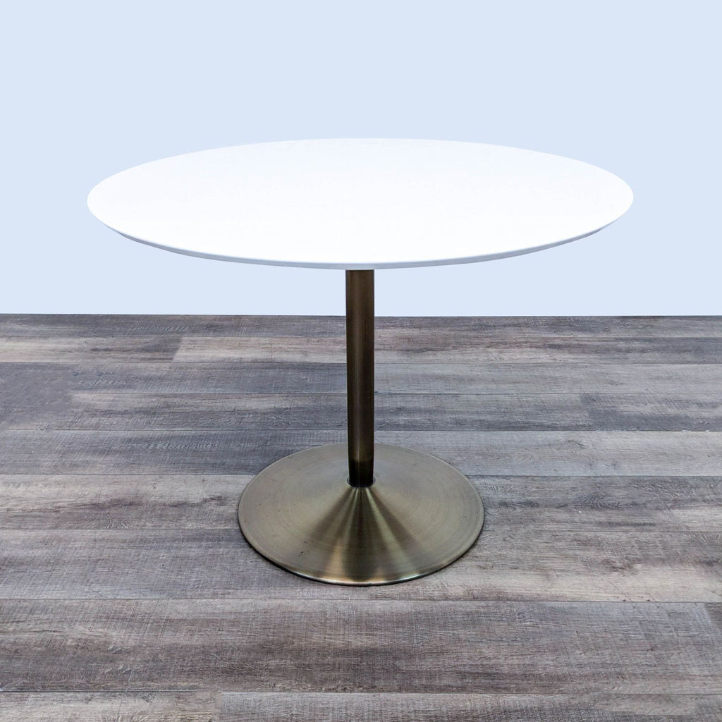 White lacquered dining table by CB2, featuring a brass-plated pedestal base on wooden flooring.  