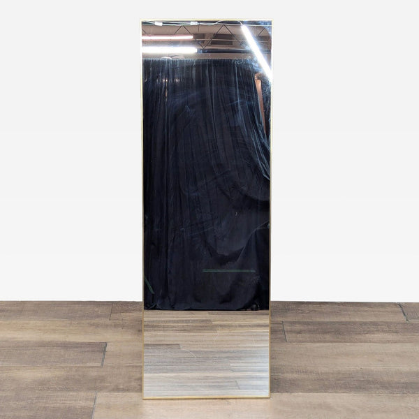 Standing mirror with gold metal frame and easel back on wooden floor.