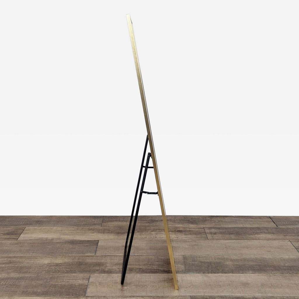 Side view of standing mirror, gold frame, easel back, wooden floor.