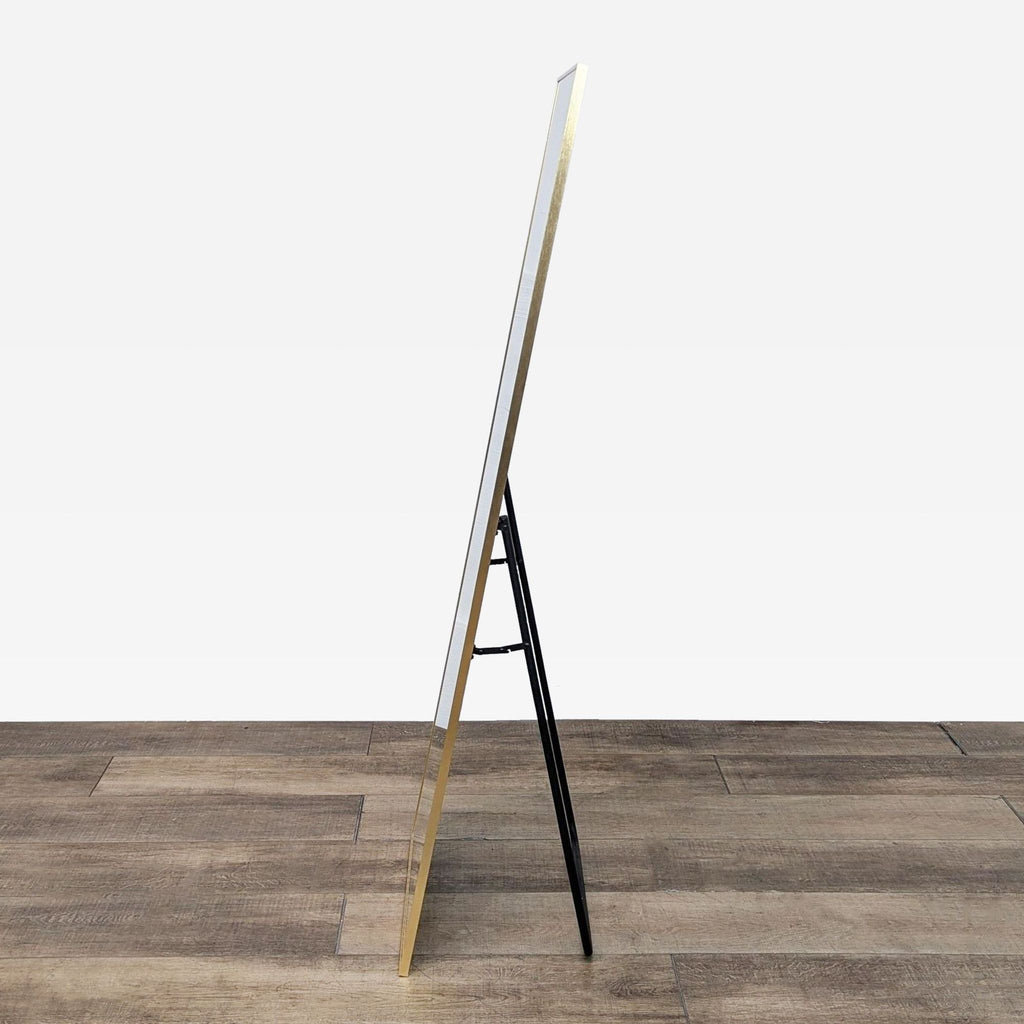 Profile view of gold-framed mirror with easel back on wood surface.