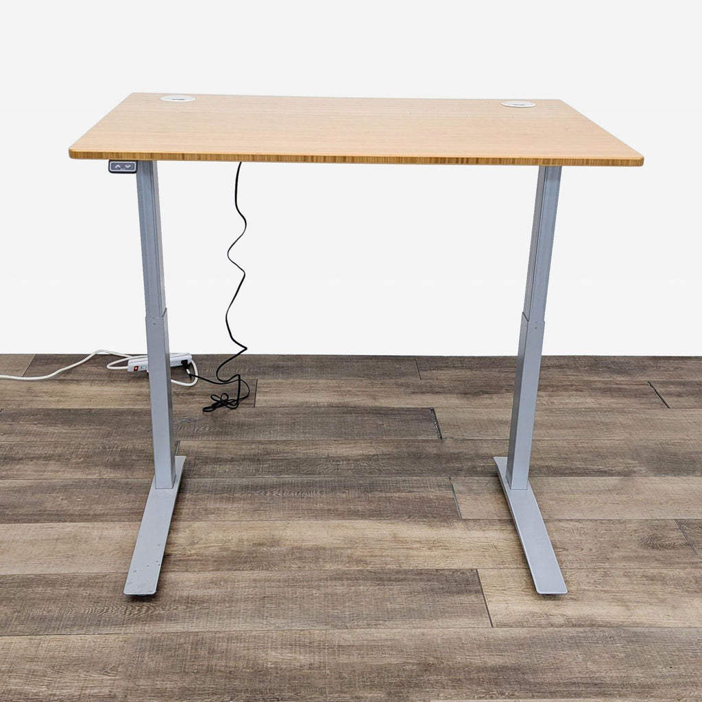 Reperch desk in raised position, wood top, gray legs, on a wood floor with visible cables.