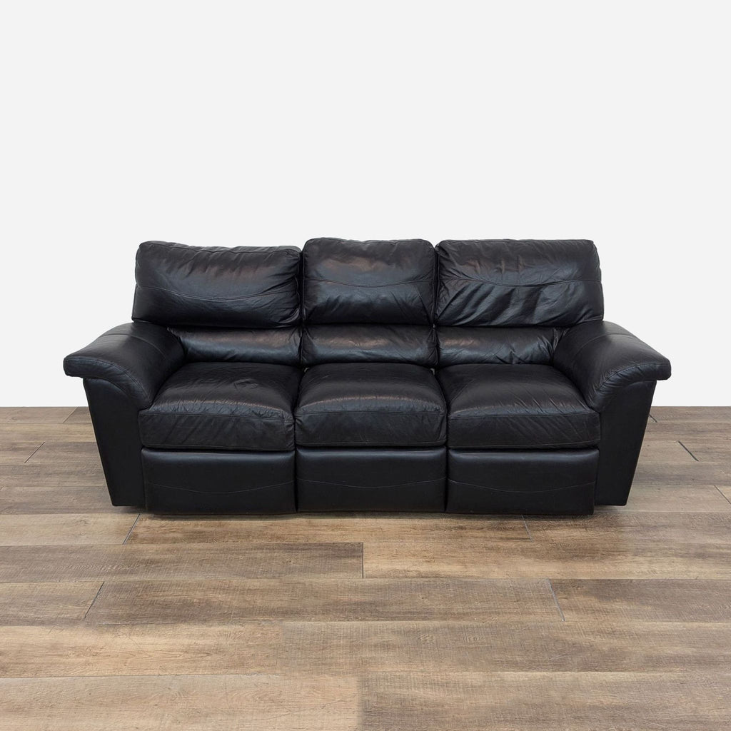 a black leather sofa in a room with a wooden floor.