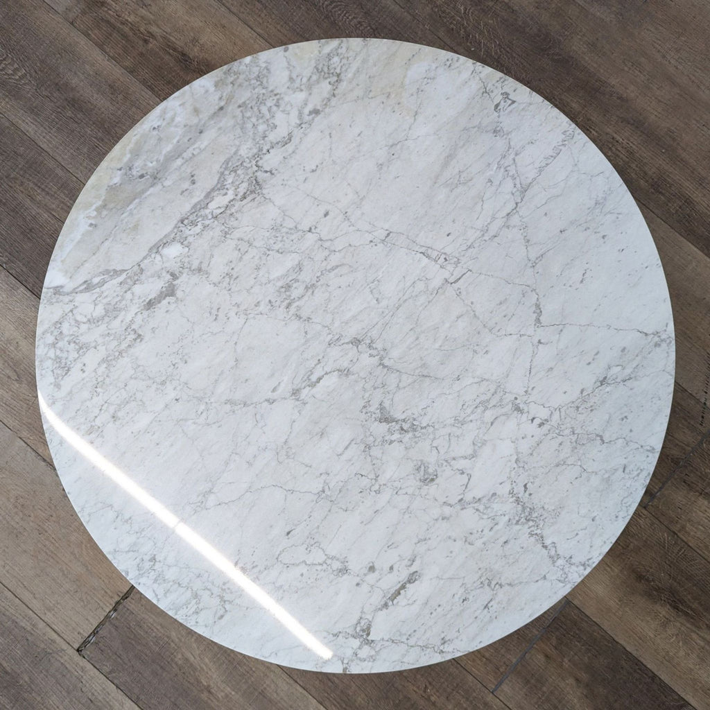 a round marble table with a light wood flooring.