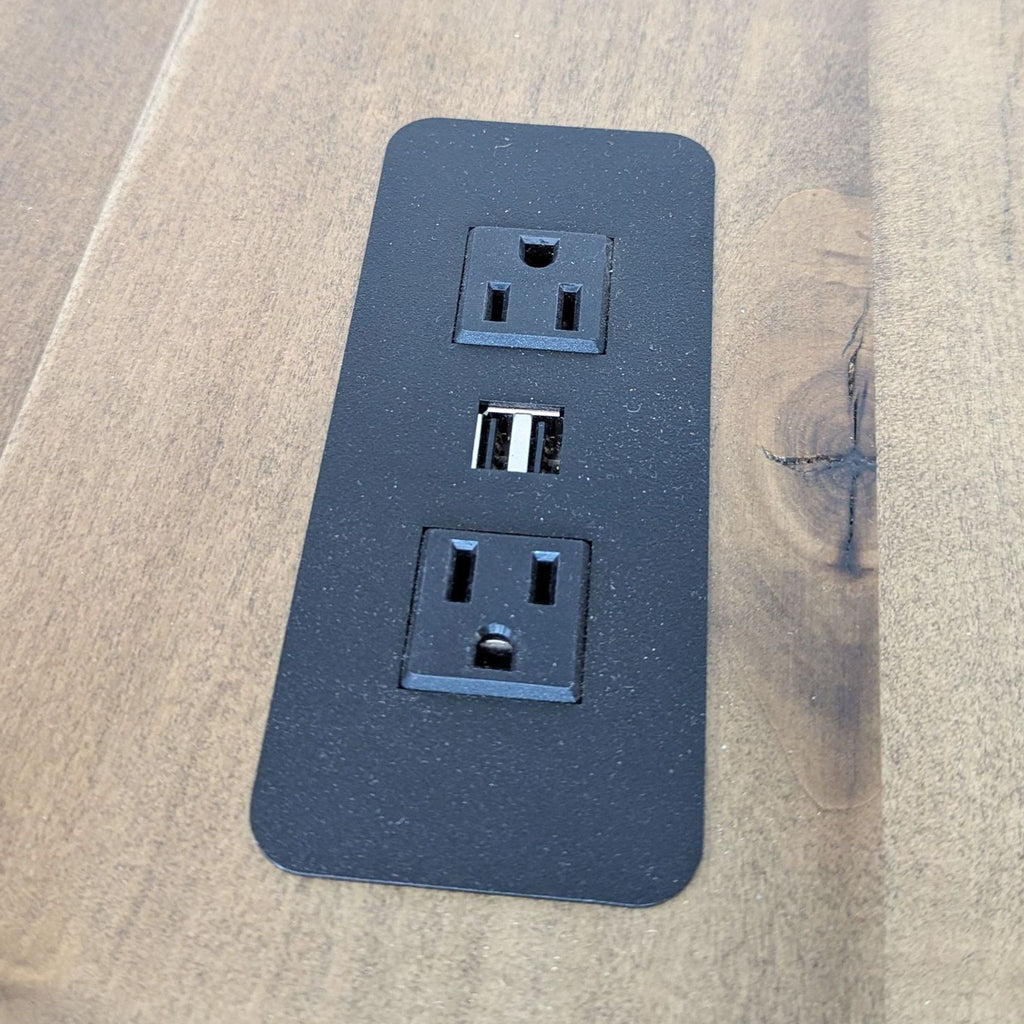 a close up of a black wall outlet with three outlets on a wood surface.