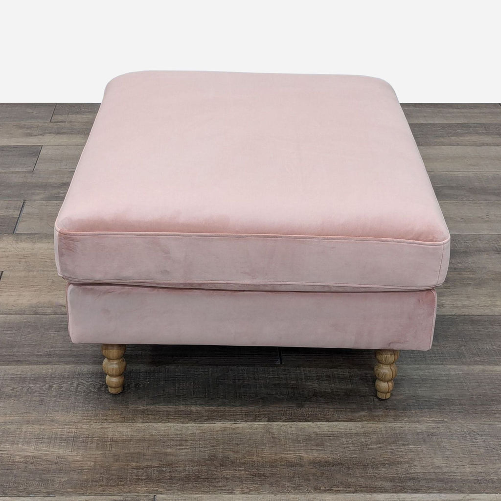 a pink velvet ottoman with a wooden base