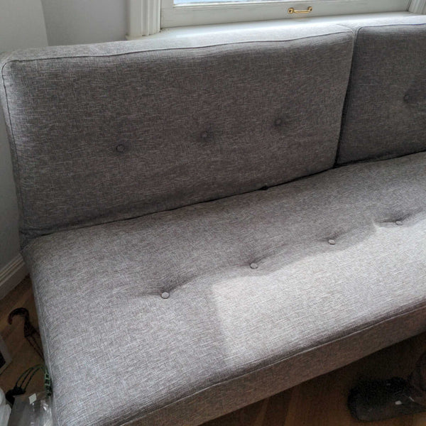 1. Close-up of a light gray sleeper sofa with button-tufted back and seat cushions near a window.