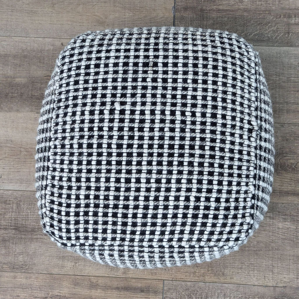 a black and white wool ottoman on a wood floor.