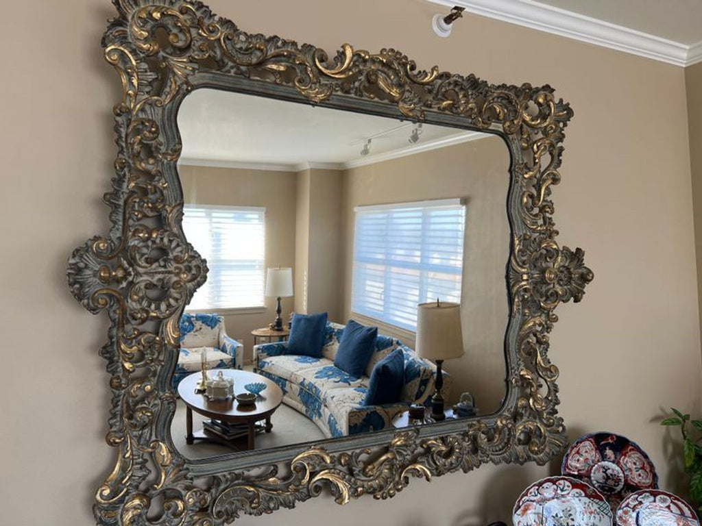 1. Ornate rectangular mirror with gold-accented, carved frame reflects a decorated living room scene.