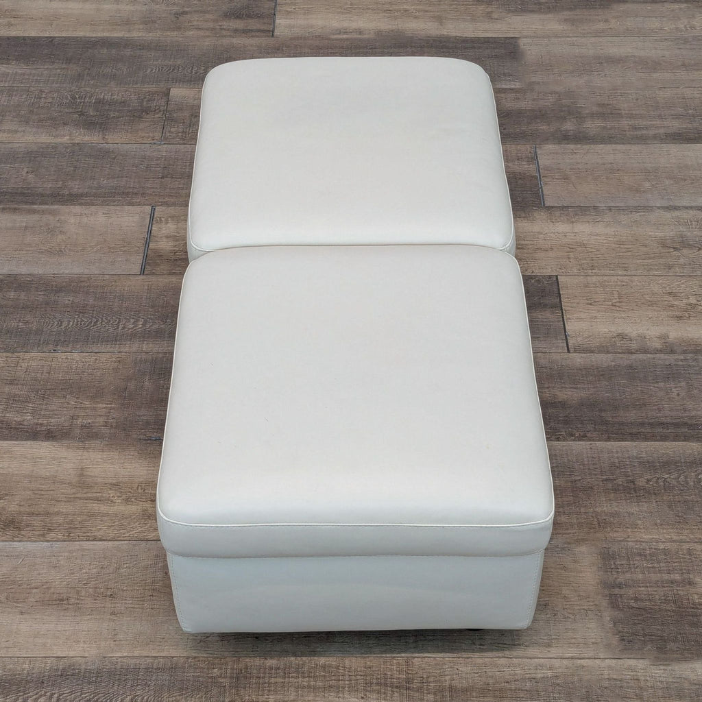 a pair of white leather ottomans on a wood floor.