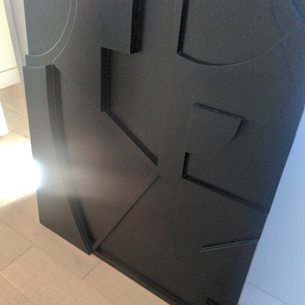 1. Close-up of a black CB2 wall art panel with geometric patterns and a matte finish, placed on a light wood floor.