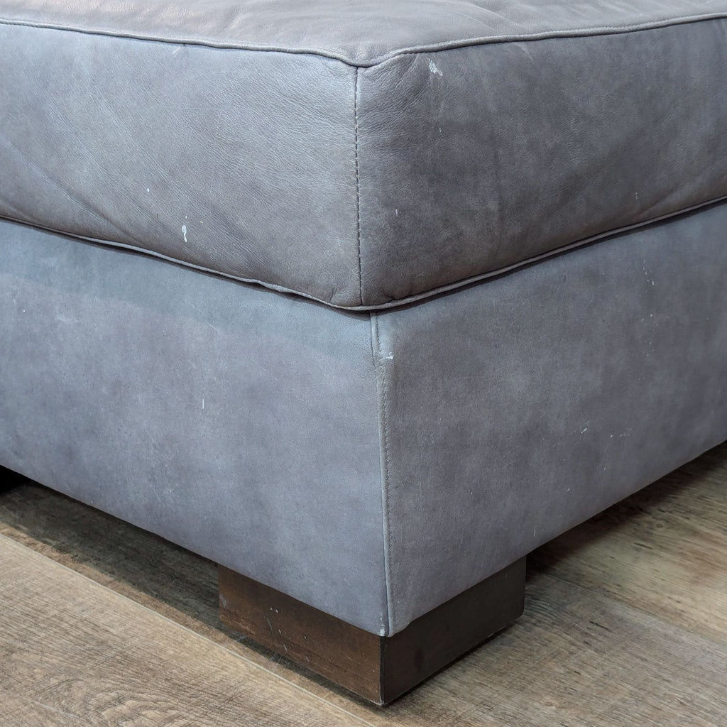 a close up of a grey velvet ottoman with a wooden base.